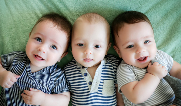 Photo of three infants one pulling sock to mouth
