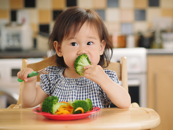 Photo of young child eating broccoli