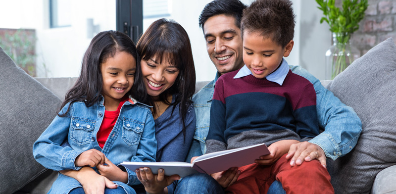 Photo of family sitting on a couch reading a book.